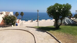 A paved pathway leading to a terrace with a view of the sea, palm trees, and a building with a sloped roof. - Coastal Escape with Backyard Beach, Inema INES (Lagos)