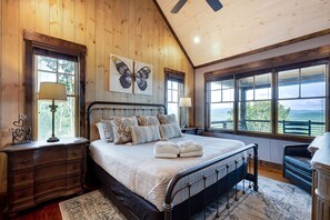 A bedroom with a large bed, wooden walls, two windows with views, and a ceiling fan. - Daybreak Ridge - Blue Ridge, GA. (Blue Ridge)