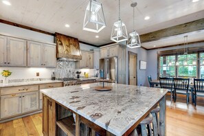 A spacious kitchen with wooden cabinets, a large marble island, and pendant lighting.