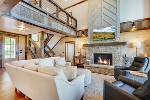 A spacious living room with a stone fireplace, a large sectional sofa, and a high ceiling with exposed beams.