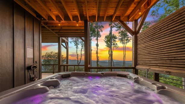 Een jacuzzi met uitzicht op een zonsondergang en bomen.