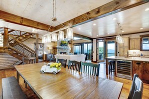 A spacious kitchen with a central island, wooden beams, and a large dining table with chairs.