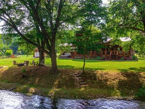 A rustic cabin with a stone foundation, surrounded by a well-maintained lawn and trees. - Take Me to the River – Blue Ridge, GA (Blue Ridge)