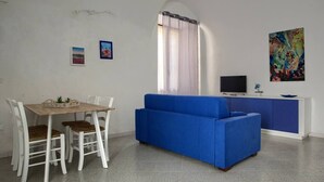 Una sala de estar moderna con un sofá azul, una mesa de comedor de madera con sillas, un televisor y un cuadro en la pared.
