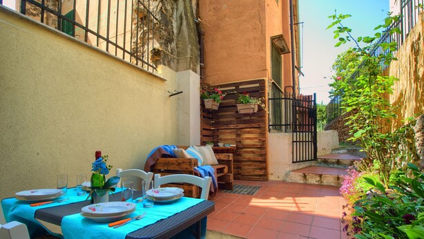 Un patio al aire libre con una mesa lista para comer, rodeado de muebles de madera y un pequeño rincón con asientos.