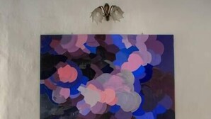 Un dormitorio con un cuadro abstracto grande en la pared, una cama con almohada a rayas y lámparas de noche.