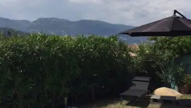 Une piscine à la forme incurvée, avec une eau d’un bleu cristallin, entourée de verdure et offrant une vue sur des montagnes lointaines.