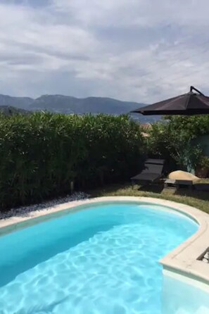 Una piscina curva con agua azul cristalina, rodeada de vegetación y con vistas a montañas distantes.