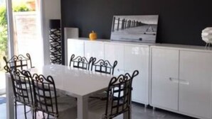 Un espace de salle à manger moderne avec une table blanche et des chaises en métal, un mur noir et une fenêtre donnant sur un paysage verdoyant.