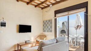 A living room with a sofa, a television, a wicker chair, a table, and a view of an outdoor patio. - Apartment 'Clara 1' close to the Sea with Terrace & Wi-Fi (Conil)