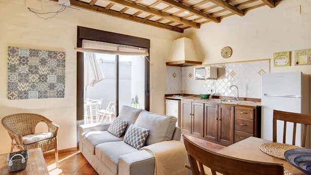A cozy living room with a sofa, a dining table, and a kitchen area with cabinets and a refrigerator. - Apartment 'Clara 1' close to the Sea with Terrace & Wi-Fi (Conil)