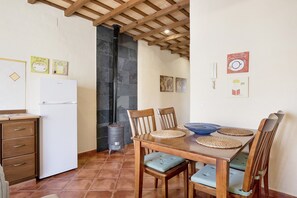 Une cuisine avec un réfrigérateur blanc, une table à manger en bois avec des chaises et un mur en pierre.