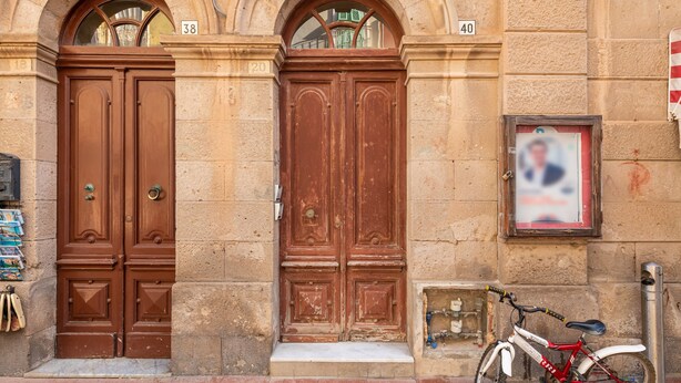 Una doppia porta in legno con un piccolo gradino che conduce all'ingresso a livello strada, una bicicletta parcheggiata all'esterno e un dissuasore metallico a destra.