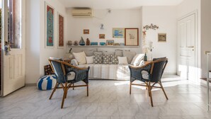 Un soggiorno con divano, due poltrone in vimini, un tavolino e una parete decorata con quadri e una piccola mensola.