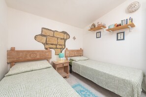 Une chambre avec deux lits, une peinture murale, des étagères remplies de livres et d’objets décoratifs, et une petite table de chevet en bois avec une lampe.