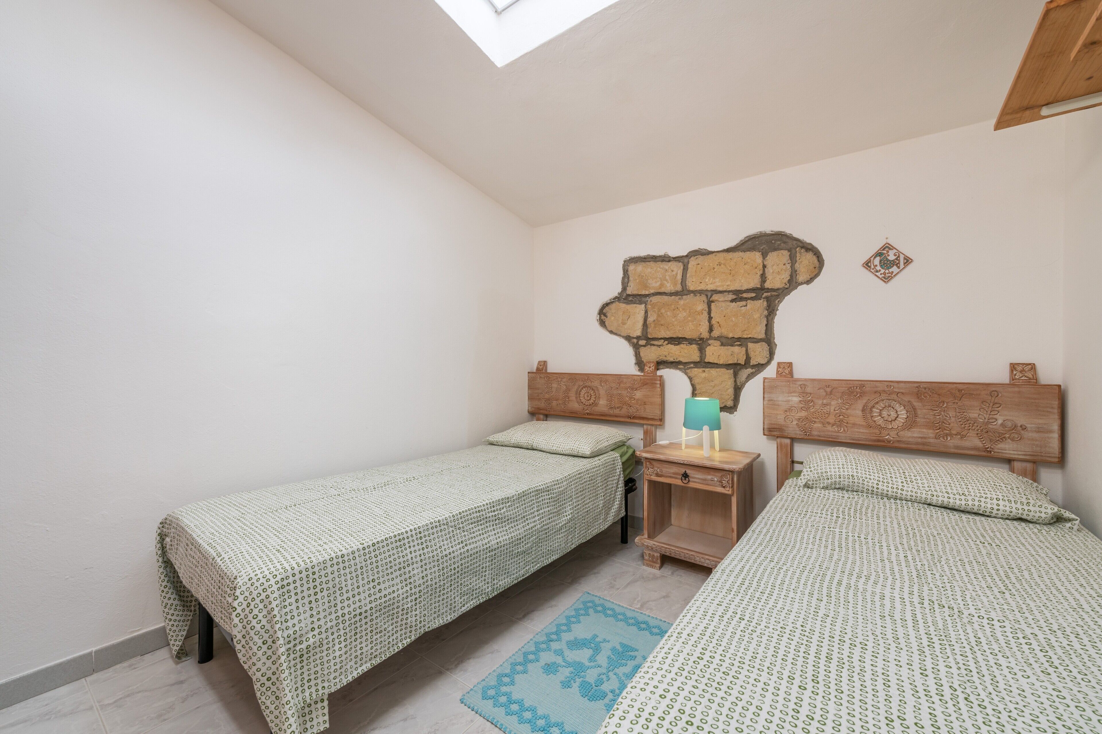 Un dormitorio con dos camas individuales, una mesita de noche de madera, un estante en la pared y un tragaluz.