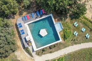 An aerial view of a swimming pool with a deck area, surrounded by greenery.