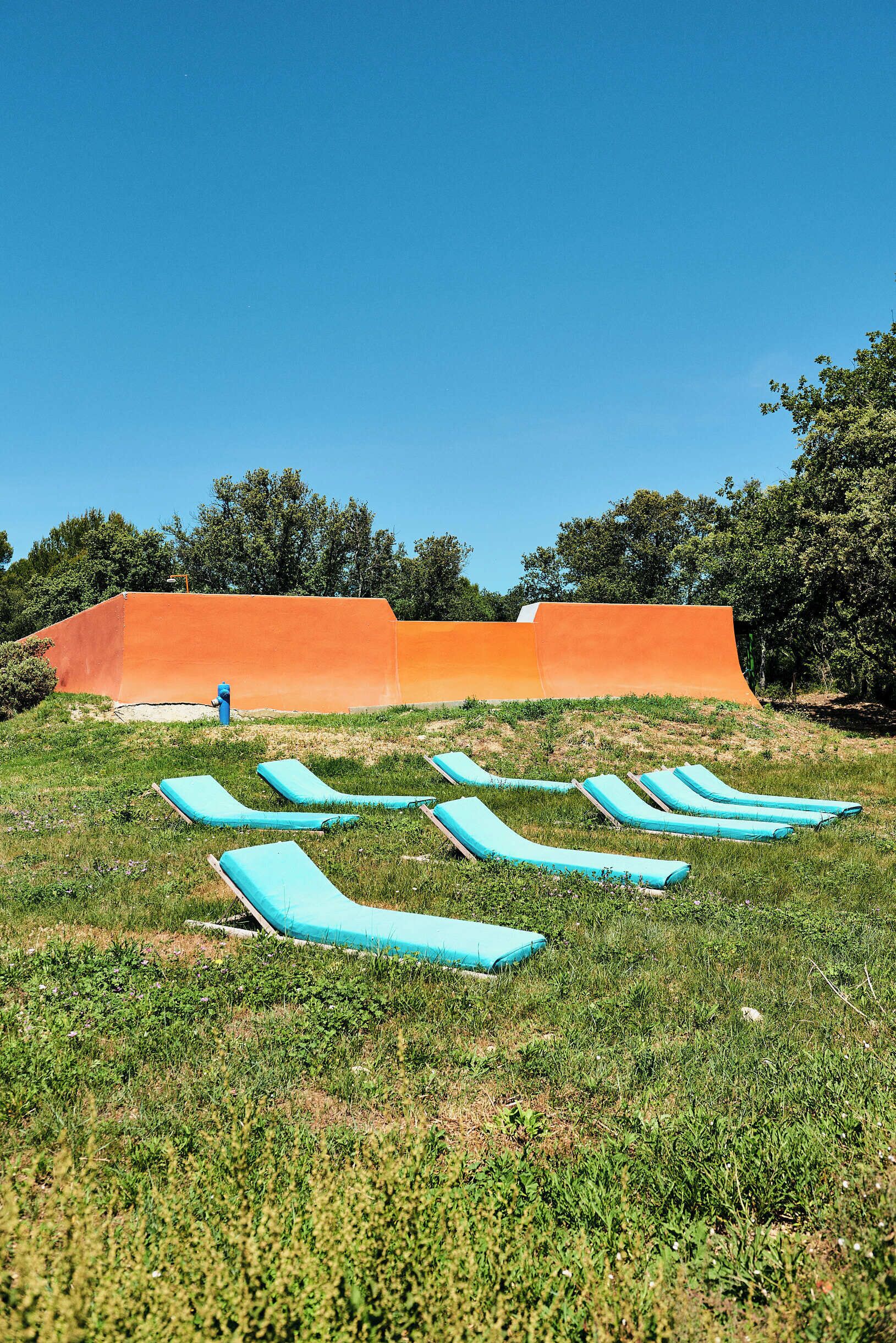 A grassy area with several blue lounge chairs and an orange structure in the background.