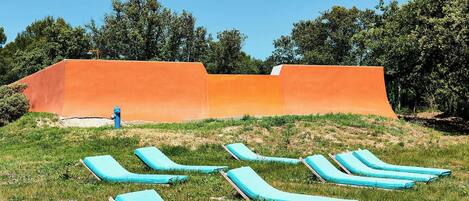 A grassy area with several blue lounge chairs and an orange structure in the background.