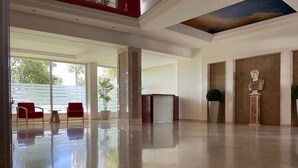 Un lobby amplio con mostrador de recepción, sillas rojas, una planta en maceta y piso de mármol.