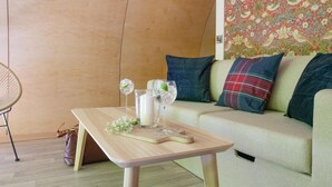 Un salon moderne avec une table basse en bois, deux verres contenant une boisson claire et une plante décorative. Un canapé avec des coussins à motifs se trouve à l’arrière-plan.