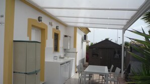 A covered patio with a dining table and chairs, a kitchen area with a white countertop and cabinets, and a small shed in the background. - Villa 'Nala' with Pool and Wi-Fi (Mazarrón)