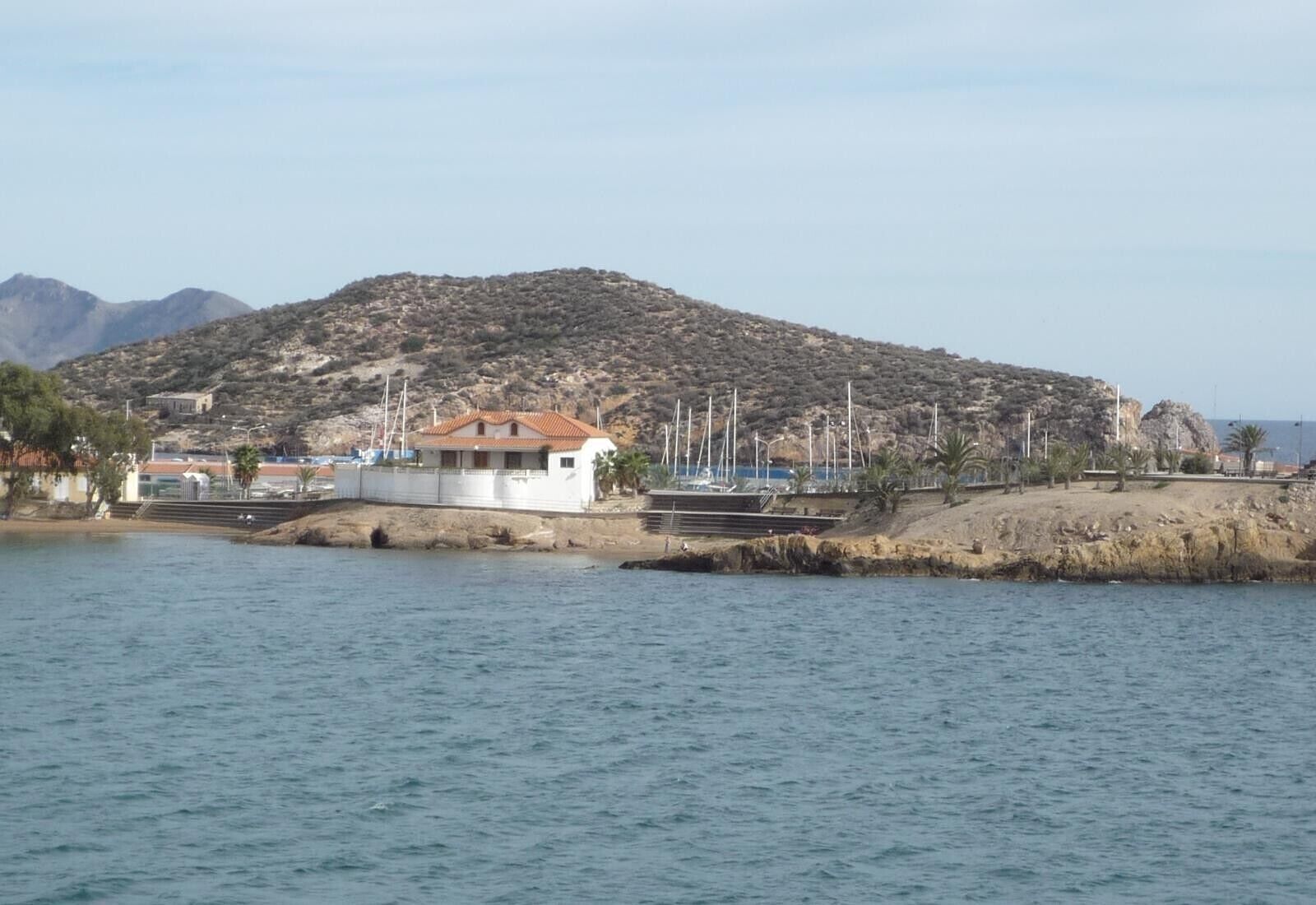 A coastal property with a white building, a rocky hillside, and a marina with boats.
