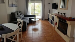A living room with a sofa, a dining table, a TV, and a fireplace. - Villa 'Capricho' with Mountain View, Pool and Wi-Fi (Mazarrón)