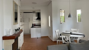 A modern kitchen with white cabinets, a dining area with a white table and chairs, and a grey sofa. - Villa 'Capricho' with Mountain View, Pool and Wi-Fi (Mazarrón)