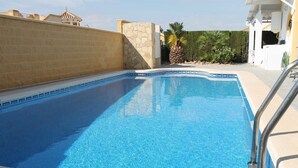 A rectangular swimming pool with clear blue water, surrounded by a stone wall and a white building with a balcony. - Villa 'Capricho' with Mountain View, Pool and Wi-Fi (Mazarrón)