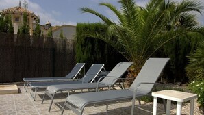A patio with four lounge chairs and a small table, surrounded by a stone floor and palm trees. - Villa 'Capricho' with Mountain View, Pool and Wi-Fi (Mazarrón)