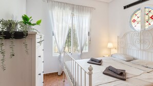Un dormitorio con cama, cortinas, una ventana con vistas, una lámpara de noche y un reloj en la pared.