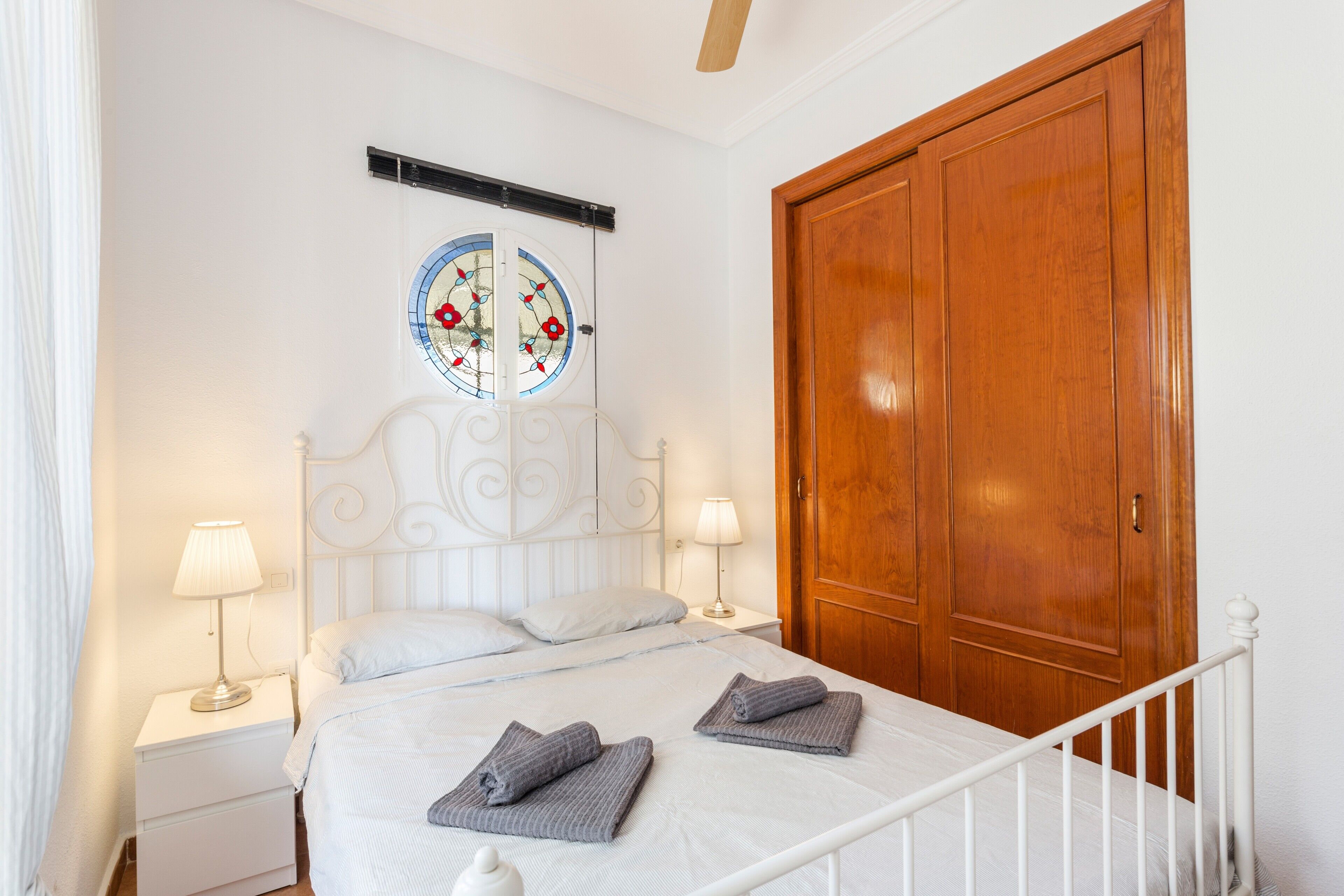 Une chambre à coucher comprenant un lit, deux tables de chevet avec des lampes, une armoire en bois et un élément décoratif mural.