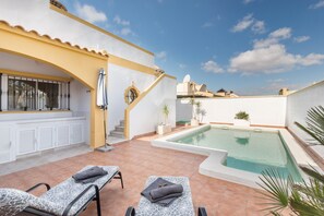 A rooftop pool area with two lounge chairs, a small pool, and a staircase leading to an upper level.