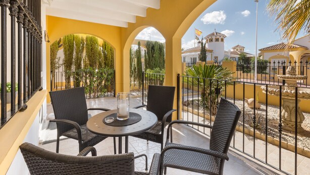 Un balcón con sillas de mimbre, una mesa con vela y vistas a un edificio con una bandera.