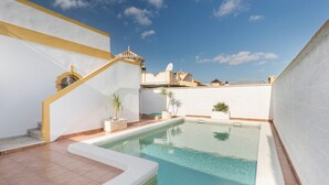 Una piscina con agua cristalina azul, rodeada de paredes blancas y una escalera que lleva a un balcón.