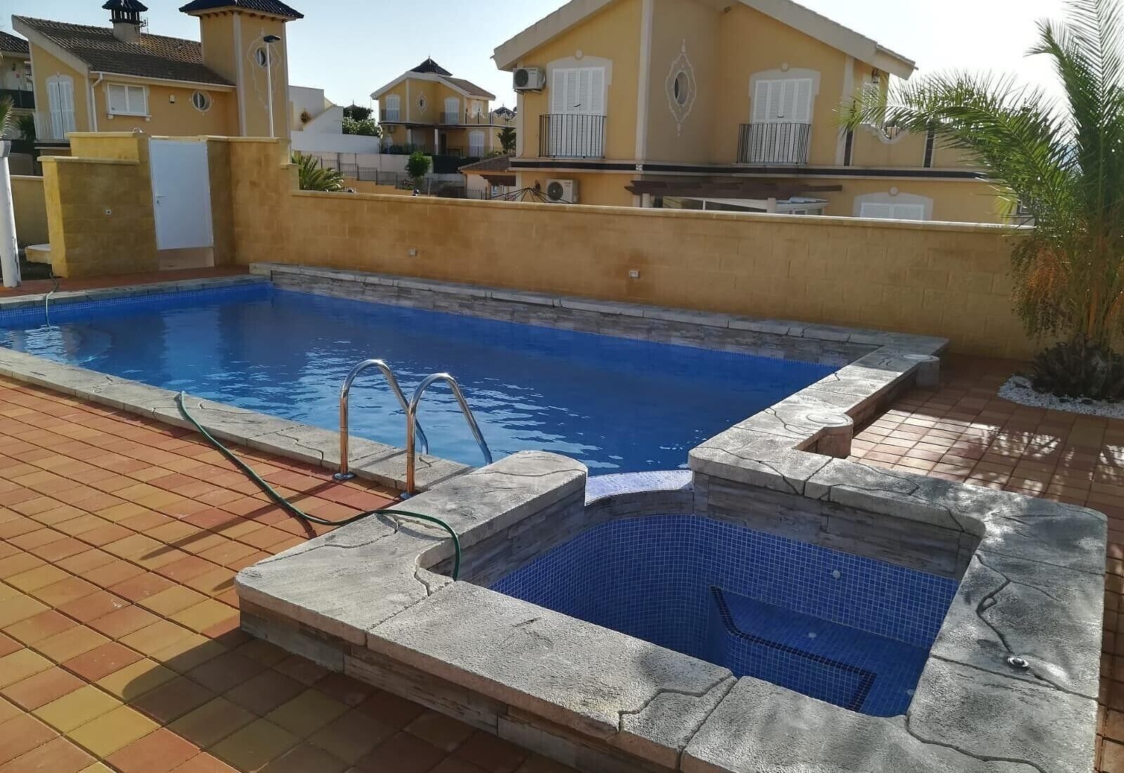 Una piscina con borde de piedra, un suelo de baldosas y un jacuzzi pequeño.