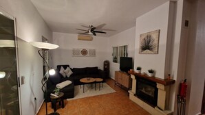 Un salon comprenant un canapé, deux petites tables, une cheminée, un ventilateur de plafond et un téléviseur.