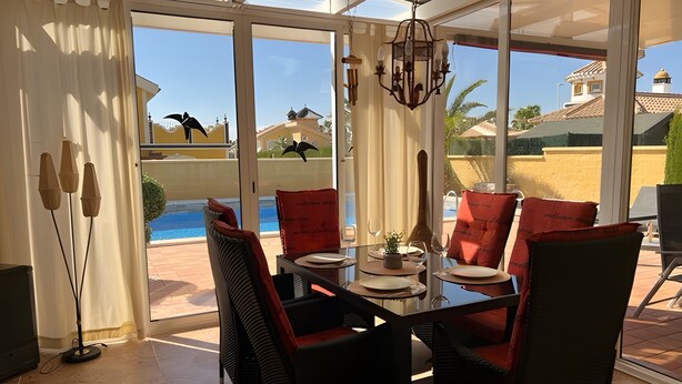 Une terrasse ensoleillée avec une table à manger, des chaises et une vue sur une piscine et des bâtiments.