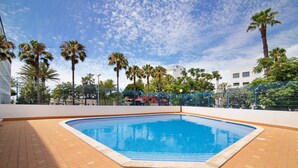 Une piscine dotée d’une terrasse carrelée, entourée de palmiers et d’une clôture.
