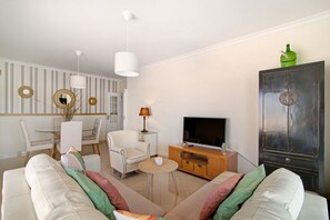 Un soggiorno con divano, poltrone, televisore, mobile contenitore e zona pranzo con tavolo e sedie.