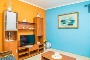 Un salon avec un téléviseur, des meubles en bois, un tableau et un ventilateur.
