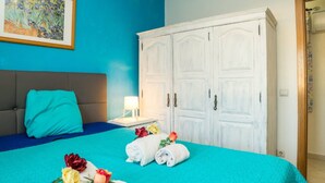A bedroom with a bed, a white wardrobe, a blue wall, and a painting. - Apartment 'T1 Anastacio' close to the Sea with Shared Pool & Wi-Fi (Albufeira)