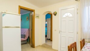 A room with a white refrigerator, a bed with a pink blanket, a dining table with chairs, and a white door with a decorative wreath. - Apartment 'T1 Anastacio' close to the Sea with Shared Pool & Wi-Fi (Albufeira)