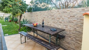 An outdoor patio with a stone wall, a wooden table with benches, and a fruit bowl. - Apartment 'T1 Anastacio' close to the Sea with Shared Pool & Wi-Fi (Albufeira)