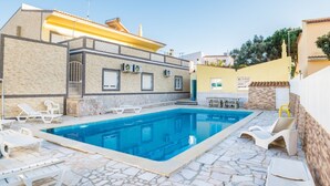 A swimming pool with lounge chairs, a stone-tiled patio, and a building with a yellow roof. - Apartment 'T1 Anastacio' close to the Sea with Shared Pool & Wi-Fi (Albufeira)