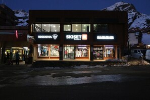 A building with multiple storefronts, including Rossignol and Skiset, with a view of snow-covered mountains in the background.