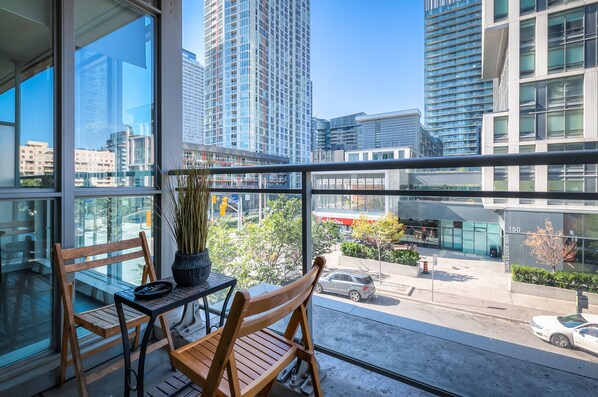 Enjoy the city view from this balcony with a bench and table, offering a clear view of the surrounding modern buildings and street.