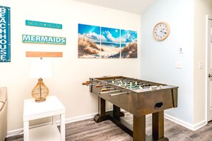 A room with a foosball table, a wall clock, and decorative signs.