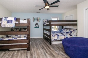 Een kamer met twee stapelbedden, een plafondventilator en een raam met jaloezieën.